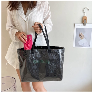Detail of glossy black patent leather tote bag with green Skillfully lettering print