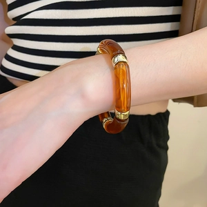 Detail view of acrylic iridescent geometric bracelet with golden metal beads on wrist