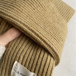 Close-up of golden brown ribbed knit hat texture with a small stitched h.mod fabric label