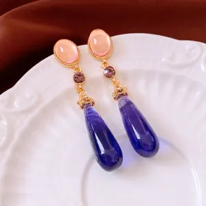 Vintage gold drop earrings with pink, purple, and blue crystals on a ceramic plate