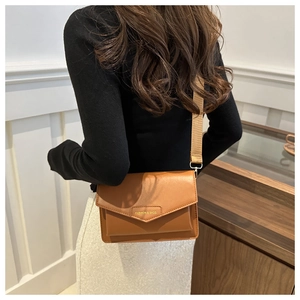 Rear view of a caramel leather crossbody bag with a wide strap on a model in black top