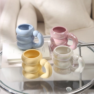 Close-up of four stacked ceramic mugs with bubble handles in pastel colors on a glass table