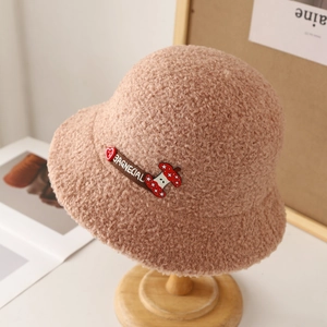 Chapeau bob en peluche beige avec broderie cœur placé sur un support en bois