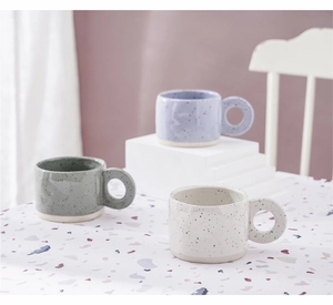 Detailed view of speckled ceramic mugs in purple, green, and white with ring handles