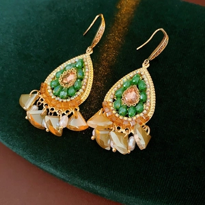 Detailed macro shot of vintage gold tassel earrings with colorful gems on green velvet