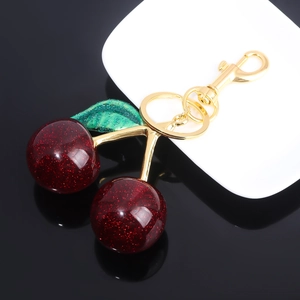 Detailed view of dark red cherry keychain with green leaves and glitter finish on gold ring