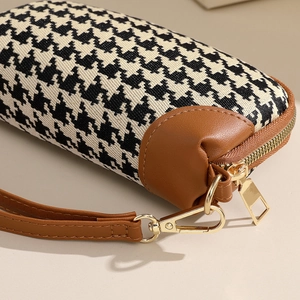 Houndstooth clutch bag with brown leather details and gold zipper in a macro view
