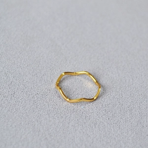 Detailed macro shot of a gold wavy geometric thin brass ring on a textured surface