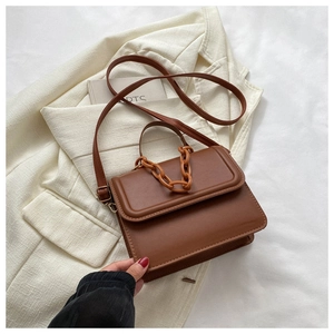 Close-up of brown leather crossbody bag with top handle and chain on white blazer