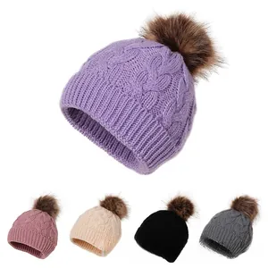 Detail view showing five colors of cable knit beanies with faux fur pom pom decorations