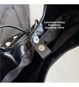 Detail of silver magnetic buckle and glossy black faux leather on the shoulder bag