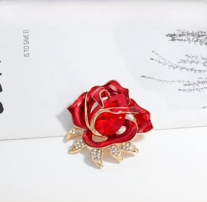 Detail of red rose brooch with crystal center and rhinestone leaves on a white surface