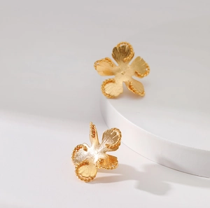 Detailed macro view of 18K gold floral earrings with matte brushed metal texture