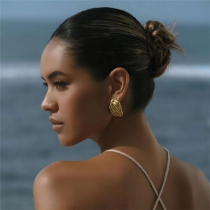Close-up of a large textured gold hoop earring worn by a model against a beach backdrop