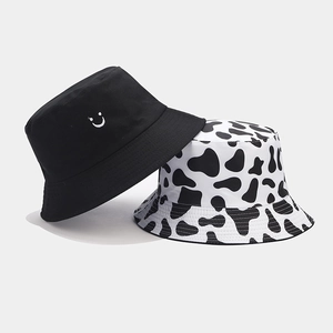 Detail view of cotton bucket hats featuring black smiley embroidery and cow print pattern