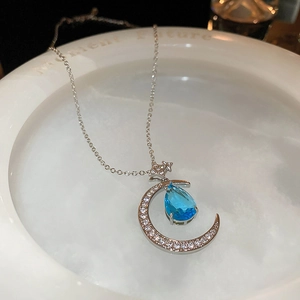 Close-up of crescent moon necklace with white zircons and a blue waterdrop gemstone