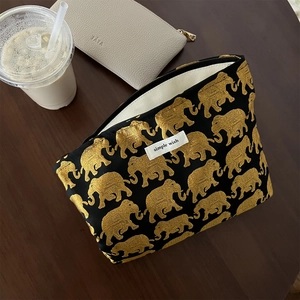 Vintage black makeup bag with golden elephant embroidery and zipper closure on wooden desk