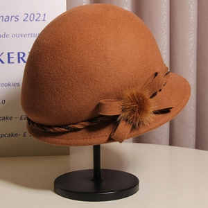 Detail of a brown wool cloche hat featuring a bow and mink fur pompom accent