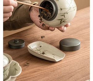 Detail showing hand pouring dry tea leaves from a bamboo ceramic jar into a matcha dish