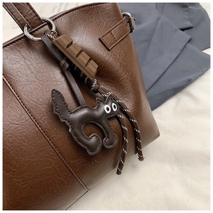 Close-up of textured brown leather tote bag featuring a cute cat and chocolate charm