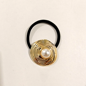 Detail showing a black hair tie with a gold circular ripple ornament and white pearl