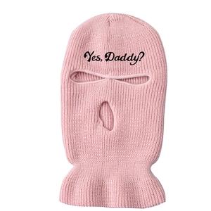 Macro view of pink knitted balaclava with 'Yes, Daddy?' black text embroidery on the forehead