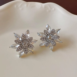 Detail of vintage-style flower stud earrings with sparkling crystals on a ceramic tray