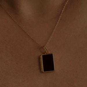 Golden shell locket necklace with black rectangular pendant shown on a female model