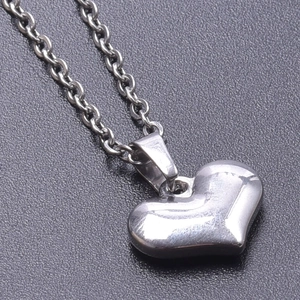 Close-up of a 3D silver heart pendant necklace with a fine chain on a textured background