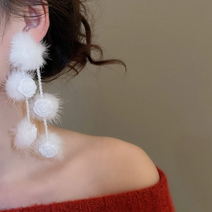 Detail of white pom-pom earrings with resin rose and beaded fringe on a red sweater