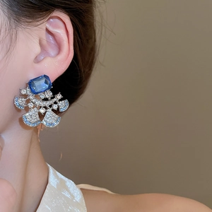 Macro shot of silver flower earring featuring a large blue gemstone and pavé diamonds