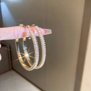 Close-up of gold hoop earrings with square zircon stones held by hand in soft light