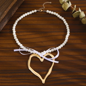 Détail d'un pendentif cœur doré et d'un collier de perles sur une surface boisée