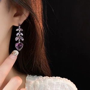 Détail de boucles d'oreilles argentées avec pierre violette en cœur sur un modèle