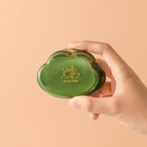 Portable cloud-shaped soap flake box in translucent green held against orange background
