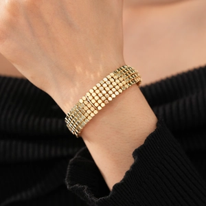 Vue détaillée d'un bracelet multicouche doré porté sur une manche en maille noire