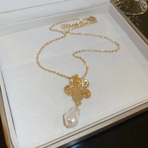 Macro shot of gold floral pendant with baroque pearl on a soft jewelry cushion
