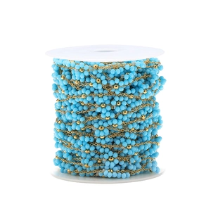 Detail of blue faceted beads and gold chain on a white spool for DIY jewelry making