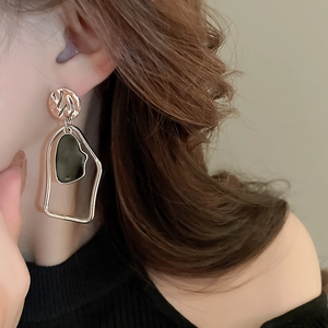 Macro detail of geometric gold earrings with textured metal and irregular green resin inlays