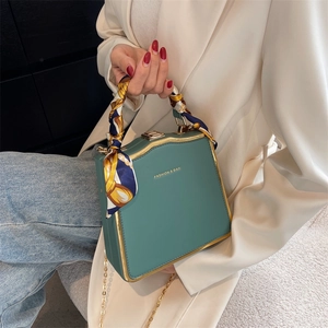 Elegant dark green box bag with gold metal frame and silk scarf handle detail