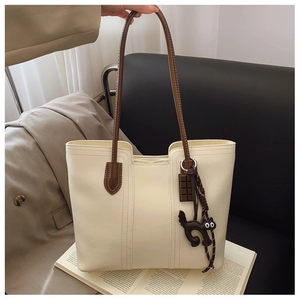 Detail of cream tote bag with brown straps, zipper closure and cute chocolate cat pendant