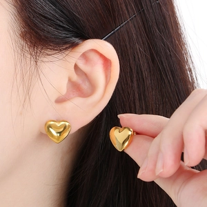 Close-up of a model wearing golden heart-shaped stud earrings in a polished finish