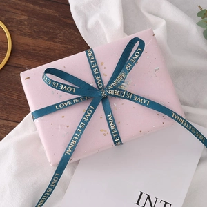 Close-up of pink gift box with gold spots and green LOVE IS ETERNAL ribbon bow