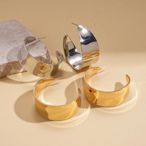 Minimalist geometric C-shaped earrings in gold and silver finish on a neutral stone display