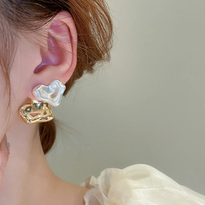 Detail view of gold irregular metal and pearl white heart-shaped earrings on a model