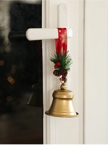 Close-up of golden Christmas bell with red silk ribbon and festive pine cone decor