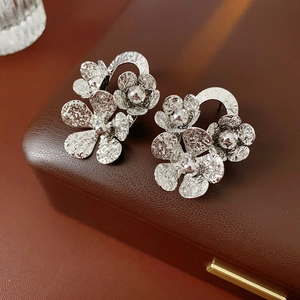 Macro detail of silver floral earrings with hammered texture on a leather gift box