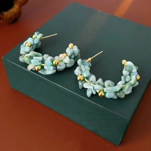 Dettaglio macro di orecchini bohémien a C con pietre blu mare su portagioie verde