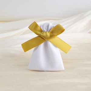 Detailed view of a white velvet drawstring gift bag with a gold ribbon bow on beige fabric