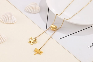 Détail du collier en acier titane doré avec perle cœur et pendentifs papillon et libellule
